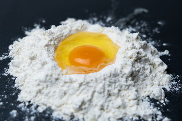 Egg breakage in white flour on a black background.

