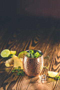 Moscow mule alcoholic cocktail in copper mug with crushed ice, mint and lemon over minton dark wooden table with amazing backlight, copy space