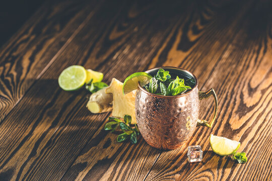 Moscow mule alcoholic cocktail in copper mug with crushed ice, mint and lemon over minton dark wooden table with amazing backlight, copy space