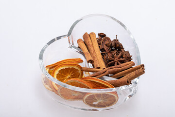 Slices of dried oranges, cinnamon and cardamom in a heart-shaped glass dish