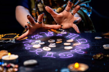 The female hands of the soothsayer read the runes. The zodiac circle glows above the runes. The concept of divination, astrology and predicting the future