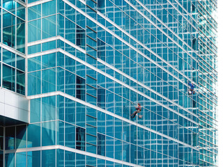 Obraz premium Two industrial climbers with safety tethers wash the glass walls of modern skyscraper. Dangerous work in the metropolis.