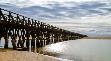 long wooden boardwalk pier leads from one beach to another over a small ocean inlet