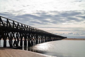 long wooden boardwalk pier leads from one beach to another over a small ocean inlet