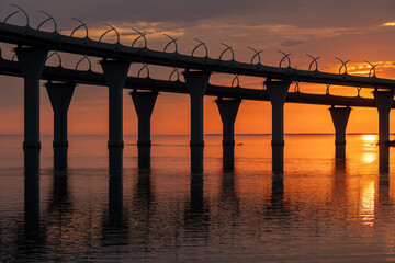 Fiery sunset on Kanonersky Island in St. Petersburg. Western high-speed diameter. Automobile bridge. The Gulf of Finland. Orange sky and reflection in the water