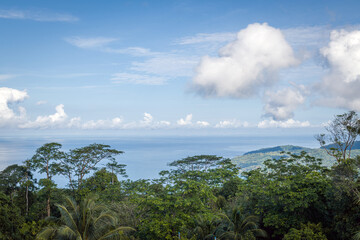 The landscape of the mountain ridge of Phuket and the Adaman Sea against the background of a blue sky with clouds.