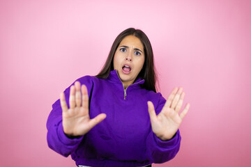 Young beautiful woman wearing sweatshirt over isolated pink background afraid and terrified with fear expression stop gesture with hands, shouting in shock. Panic concept.