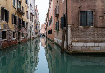 ein Kanal in San Marco, Venedig, am Horizont eine steinerne Brücke und eine italienische Fahne, die Häuserzeiten spiegeln sich im Wasser