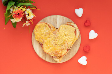 Pizza in the shape of a heart on a red background. Made with love. Happy Valentine’s Day concept. Table decorated for a romantic din