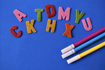 Random color letters with red blue and yellow pencils and magic markers on blue background