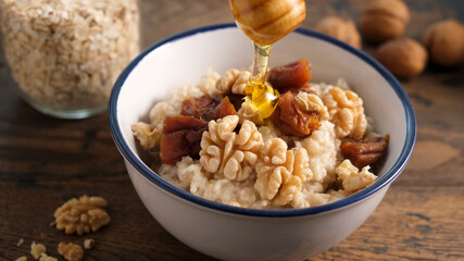 Oatmeal porridge with dried fruits and walnuts and honey. Adding honey to healthy breakfast porridge oats