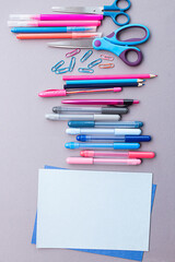 Various stationery in pink and blue colors, blank sheets of paper, on a gray background with copy space. Flat lay with pencils, scissors, pens, paper clips, felt-tip pens and sheets of paper.