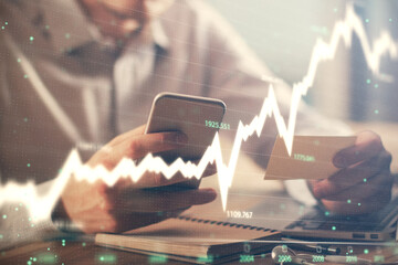 Double exposure of man's hands holding and using a phone and financial graph drawing. Analysis concept.