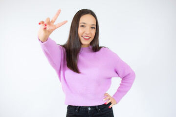 Portrait of a young funny woman in casual sweater showing peace gesture with a hand isolated over white background