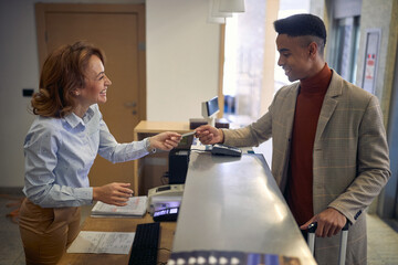 young afro-american male paying with card to a friendly female caucasian receptionist