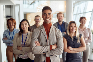 youjng afro-american businessman standing in front of his team. arms crossed, smiling, looking at...