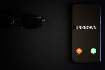 A smartphone with an unknown call lies on a dark surface next to black sunglasses. The problem of...