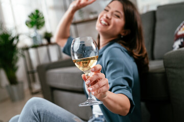 Beautiful woman sitting on the floor, drinking wine. Young woman celebrate with wine at home.
