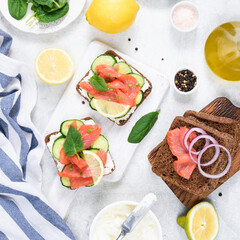 Salmon sandwiches with cream cheese, cucumber served on white wooden board, top view. Flat lay composition, square crop