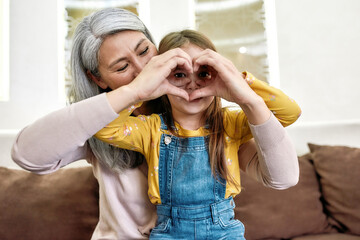 Love. Portrait of little granddaughter showing heart sign together with her loving grandmother...