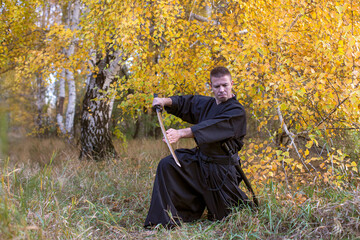 Man with sword in traditional Japanese martial art clothes training in a yellow woods.