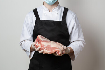 Butcher in an apron on a light background holds pork and a hatchet for cutting meat. Close-up. - 403789662