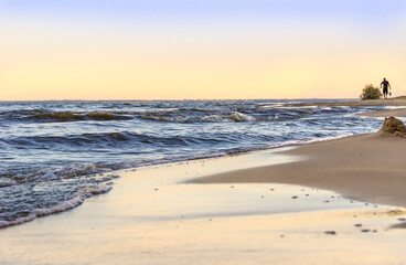 at dusk, low waves roll over the sandy shore, in the distance a person is carrying something, selective focus