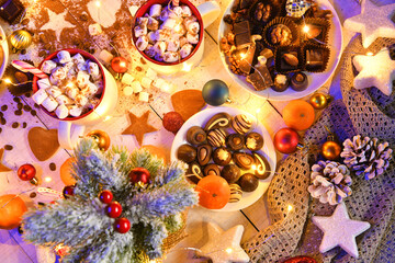 sweet food top view background for merry christmas or new year holiday decoration with night illumination - chocolate candies, tangerines, cookies, marshmallow and cocoa latte on white wood