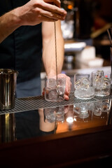 male bartender's hands mixing ice cubes with bar spoon to chill cocktail glasses