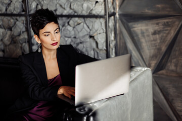 Beautiful gorgeous female boss in fashion dress sit at the sofa, using laptop. Stylish elegant...