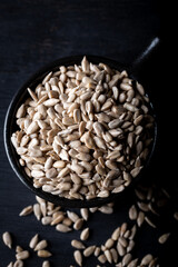 Peeled sunflower seeds in ceramic bowl on dark background. Top view.