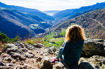 Naklejka premium Blond woman with curly hair, sitting on the mountain, looking at the fantastic views of the Ribes Valley, in the Ripolles region, Girona