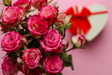 Beautiful bouquet of roses on a blurred pink background with a heart-shaped box. Valentine's Day and love concept. Greeting card. Selective focus, close-up