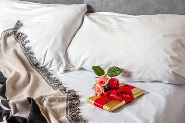 A gift box and flowers lies in bed early in the morning. Content for honeymooners and lovers for Valentine's Day.