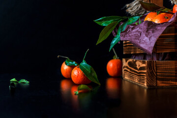 Tangerines, mandarins, clementines, citrus fruits with leaves in a wooden basket. Black background. Side view