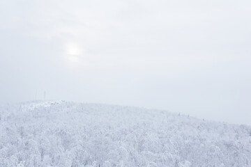 winter view to the snowy wooded hills in frosty fog, cell towers are visible in the distance