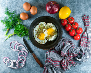 Fried eggs in a pan with pepper and thyme on a gray background, fresh tomatoes,