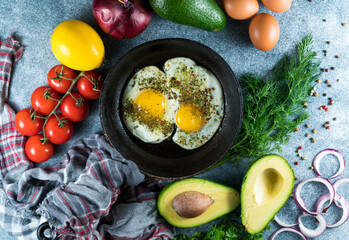 Fried eggs in a pan with pepper and thyme on a gray background, fresh tomatoes