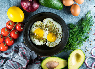 Fried eggs in a pan with pepper and thyme on a gray background, fresh tomatoes