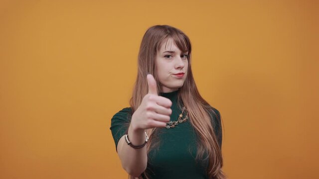 Showing thumbs up, like sign Positive something good has happened finger gesture for fine result well done. Young attractive woman, dressed green shirt blonde hair, yellow background