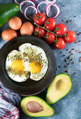Fried eggs in a pan with pepper and thyme on a gray background, fresh tomatoes,