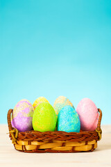 Colorful easter eggs in basket on table on blue background