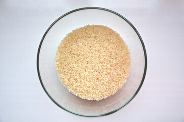 A big bowl of white rice photo from the top. Processed raw rice for cooking. Transparent bowl with yellow rice grits.