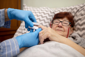 Doctor examining senior woman using oximeter at home , Oximeter test elder patient in prevention of Covid 19 pneumonia on a nursing home