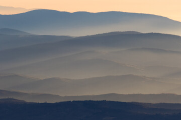 Fototapeta premium Winter in the Mountains. Beautiful orange mist or fog at sunrise time. Good sunlight and patterns in the landscape. Sea of clouds.