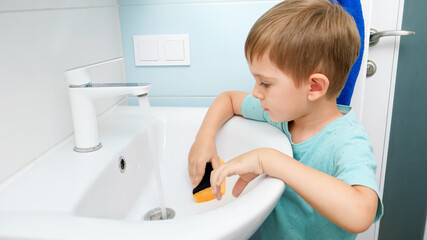 Little toddler boy washing water sink in bathroom while doing housework and helping parents