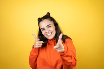 Young beautiful woman wearing sweatshirt over isolated yellow background pointing to you and the camera with fingers, smiling positive and cheerful