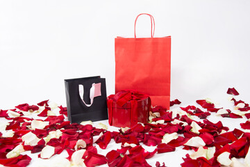 Black and red kraft paper shopping bags and gift box with bow isolated with red rose petals on white background. Valentine's day gifts.Holiday shopping.