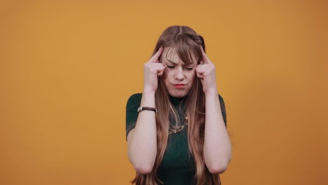 Headache grimacing pain holds the back of neck indicating location. Fatigue during workaholism labor. Young attractive woman, dressed green shirt blonde hair, yellow background