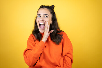 Young beautiful woman wearing sweatshirt over isolated yellow background hand on mouth telling secret rumor, whispering malicious talk conversation